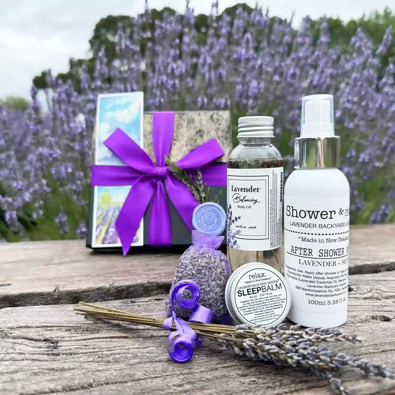 Merry Christmas! After-Shower Lavender Gift Box featuring Lavender Argan Body Oil, Lavender & Mint After-Shower Mist, Lavender Sleep Balm, Dried Lavender Sachet, Mini Lavender Dry Flower, and a Lavender Field Bookmark, displayed with the background of a lavender field in a serene lavender backyard garden.