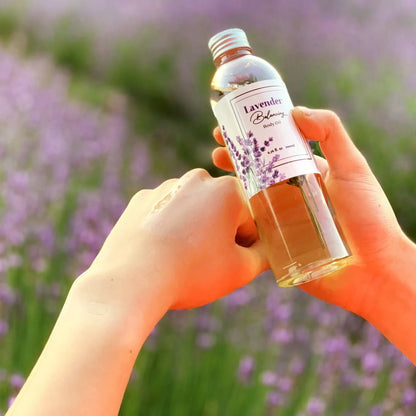 Moisturizing body oil scented with lavender essential oil, set against a sunset lavender field.