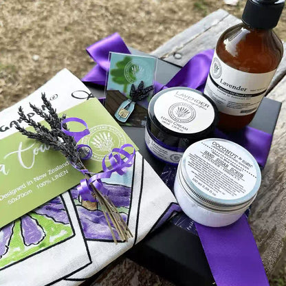 Mother's Kitchen Comforting Treat Gift Set placed on a wooden bench, featuring products such as Lavender Sugar Scrub, Lavender Hand Cream, Tea Towel, Lavender Hand Wash, Lavender Fridge Magnets, Mini Lavender Dry Flower, and Lavender Field Bookmark.