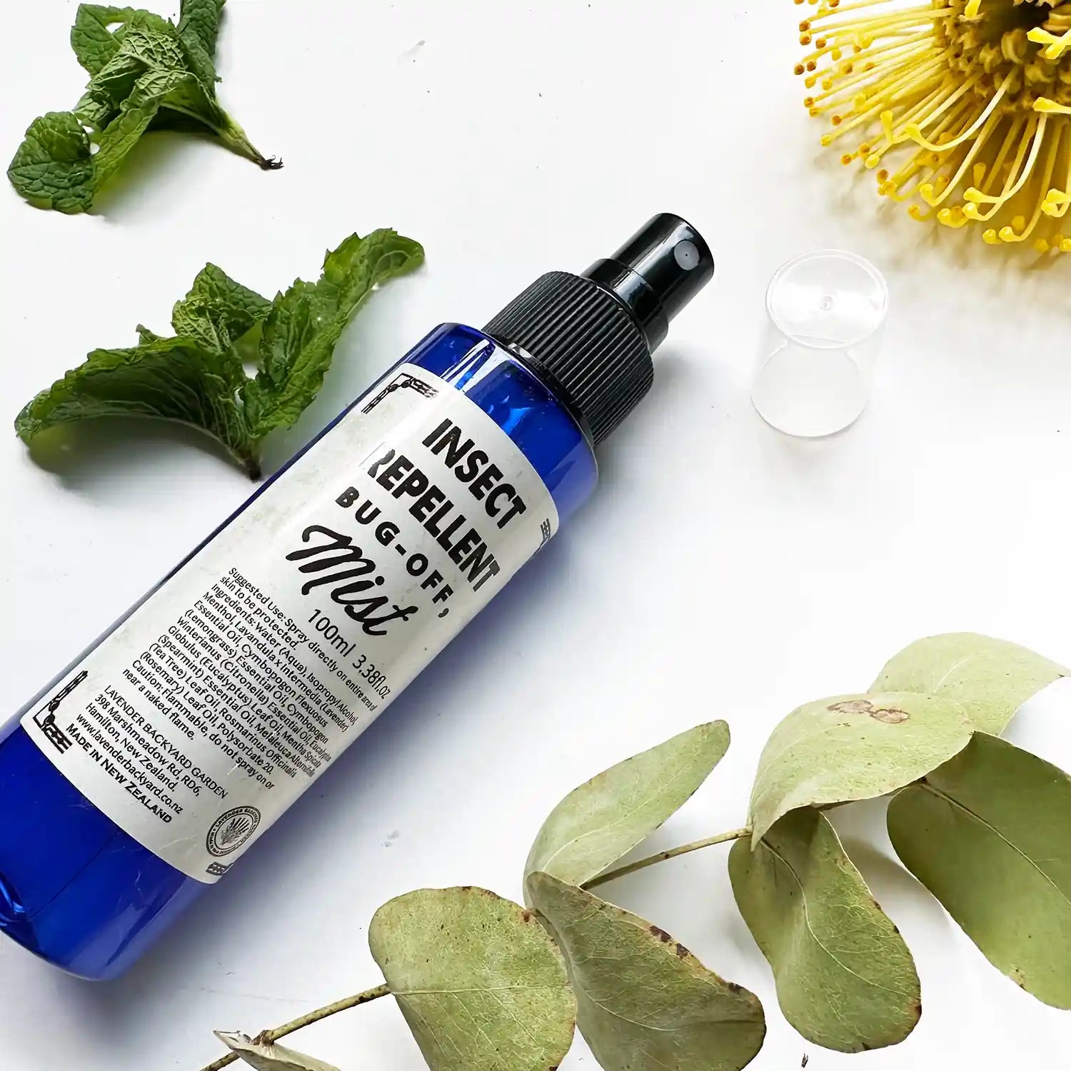 Natural insect repellent spray scented by essential oils, with a background of fresh mint leaves, eucalyptus leaves, and yellow flowers, highlighting its plant-based ingredients.