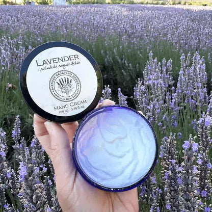 Natural lavender hand moisturiser for dry hands scented by essential oils, held by hand against a backdrop of purple blooming lavender.