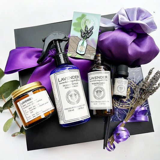 Gift set with a purple ribbon background and eucalyptus leaves, containing lavender essential oil scented coconut candle, mint and lavender room spray, lavender reed diffuser, luxury satin lavender sachet bag, a jar of lavender fridge magnet, mini dried lavender bundle, and pure lavender essential oil.