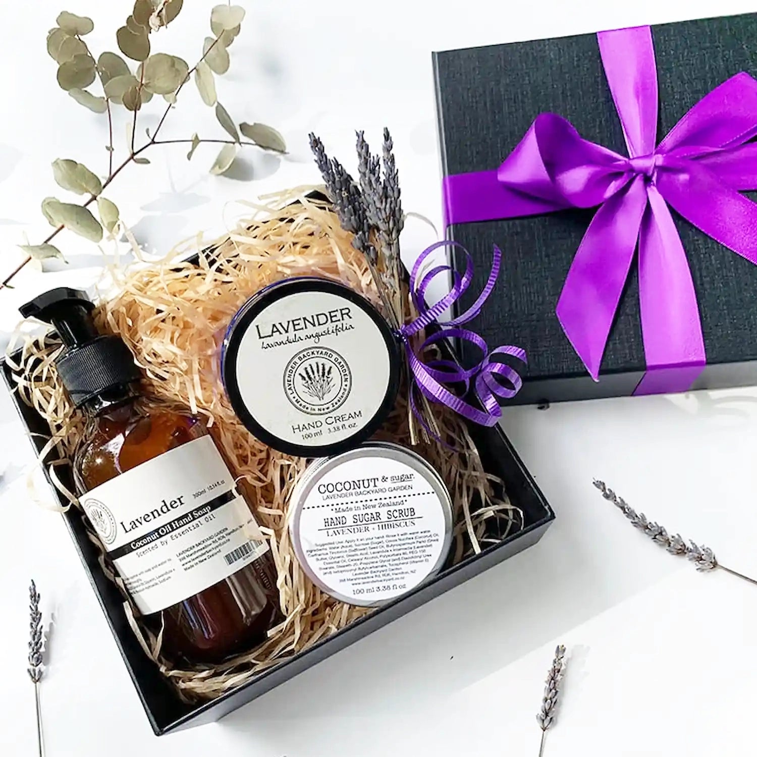 Nourishing Hand Therapy Gift Hamper featuring hand wash, hand scrub, and hand cream, all scented with essential oils, beautifully presented in a purple ribbon gift box with dried eucalyptus leaves in the background.