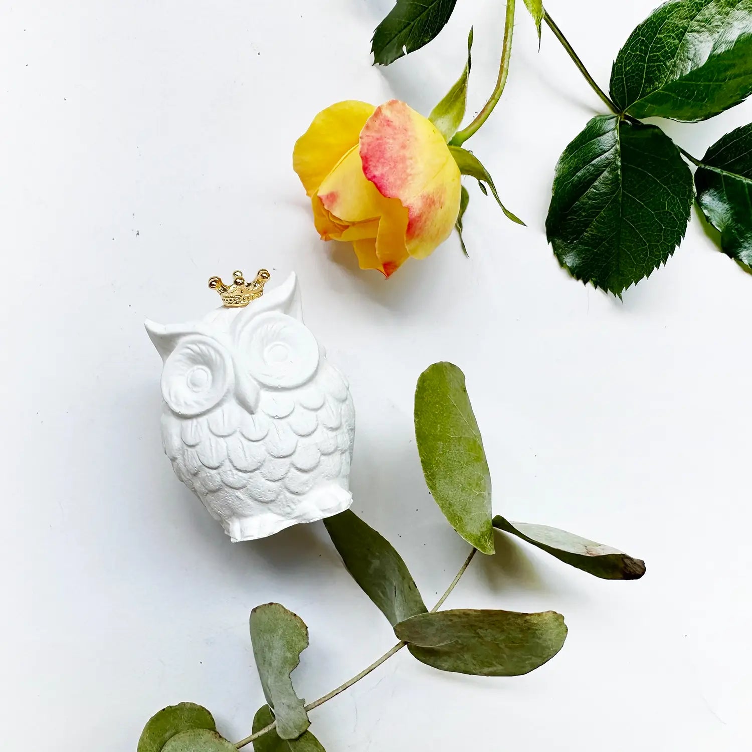 Owl aroma stone freshener decorated with eucalyptus leaves and yellow roses.