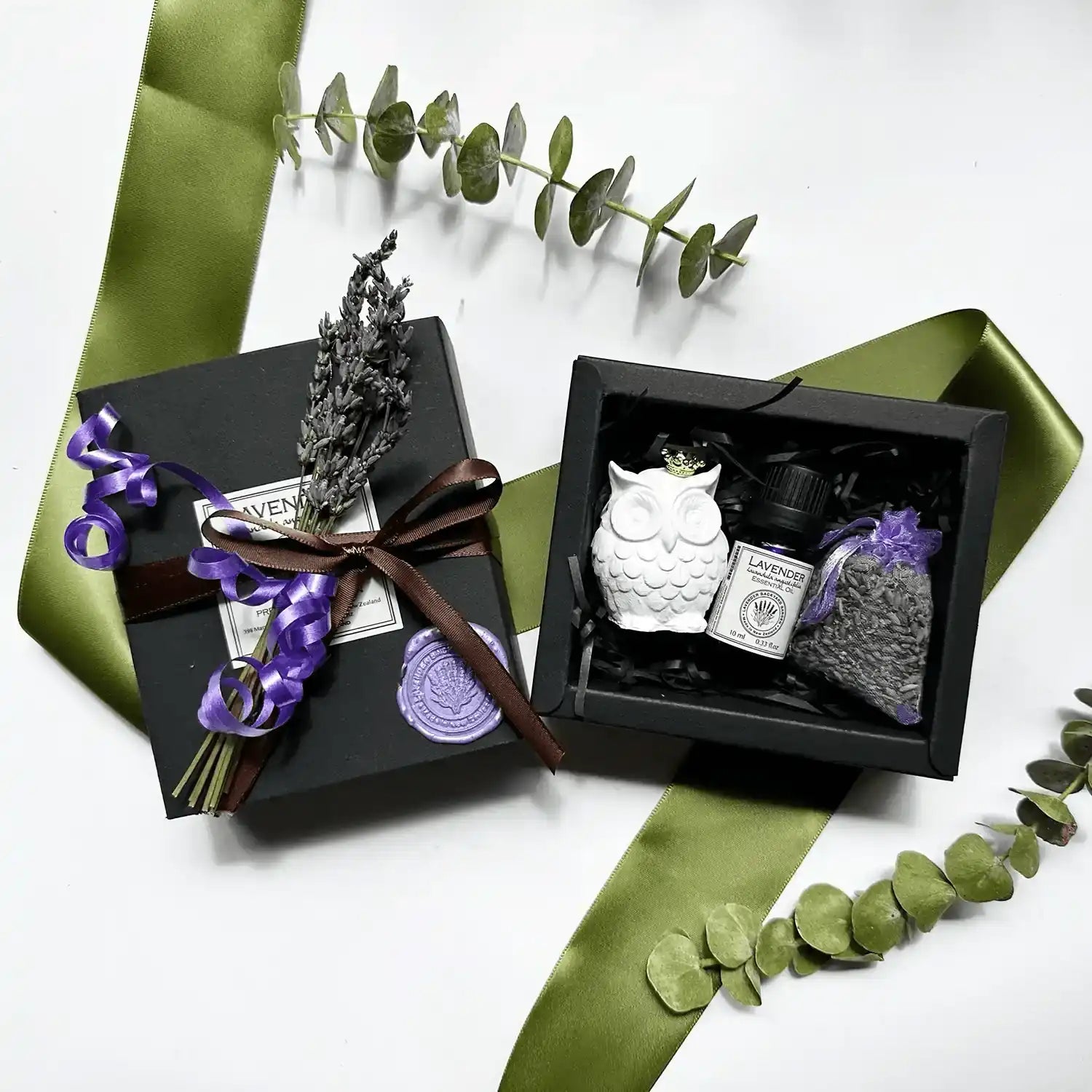 Owl & Calm Essential Oil Gift Box with a mini owl aroma stone, lavender essential oil, and a lavender sachet, packaged in a black gift box with a purple ribbon and dried lavender flowers.