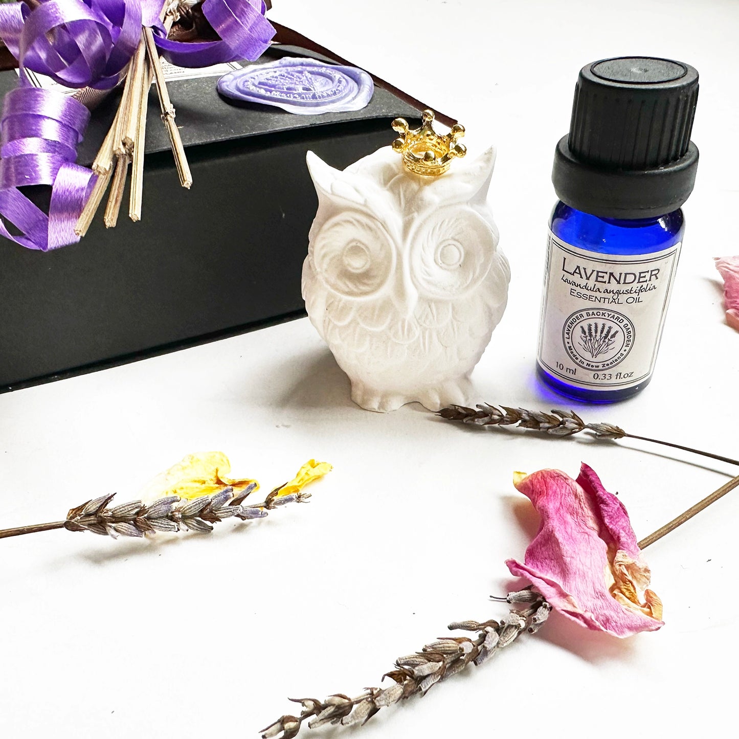 Owl gift set featuring mini owl aroma stone, lavender essential oil, and mini lavender dried flower, with dried lavender flowers and rose petals in the background