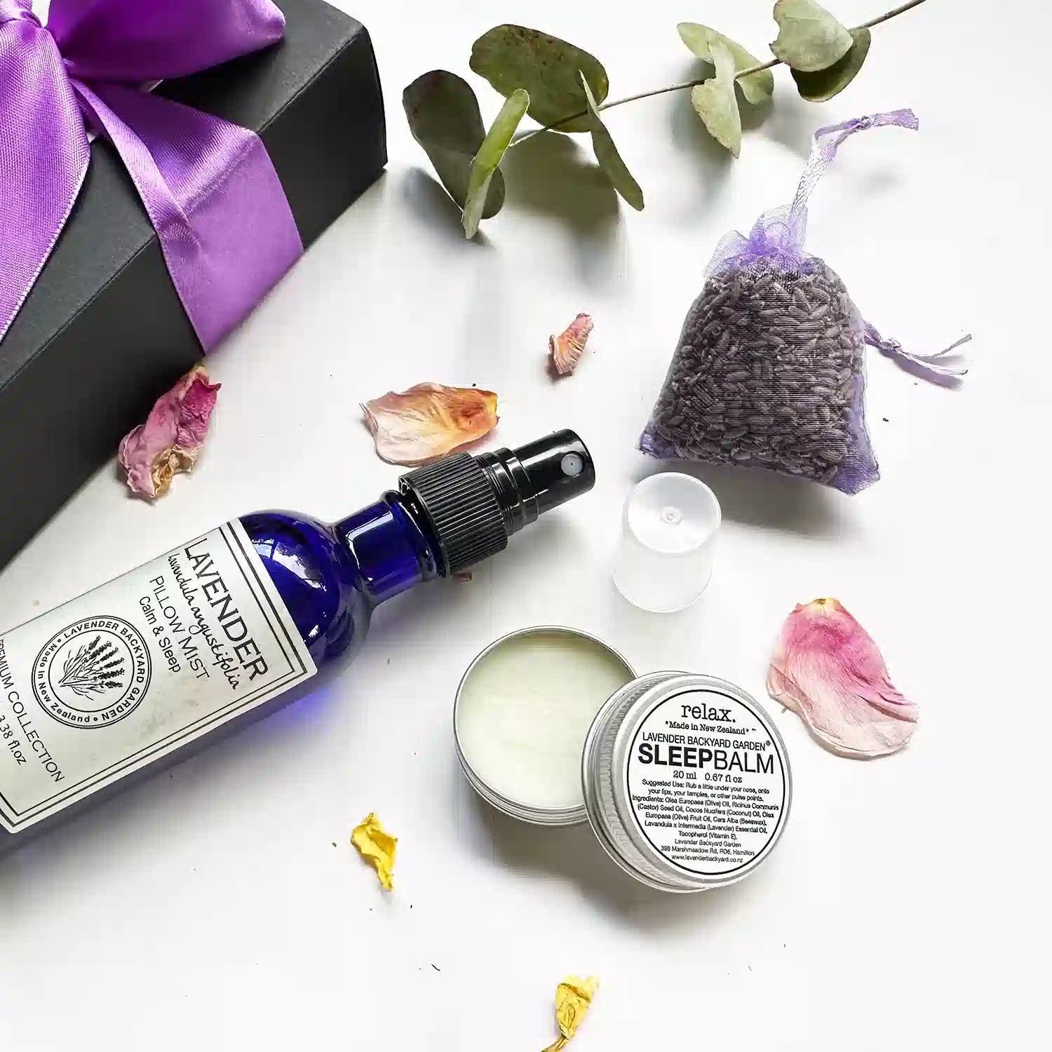  Close-up view of "Lavender Sleep Balm, Lavender Sleepwell Pillow Mist, Dried Lavender Sachet," with background decoration of eucalyptus leaves and rose petals.