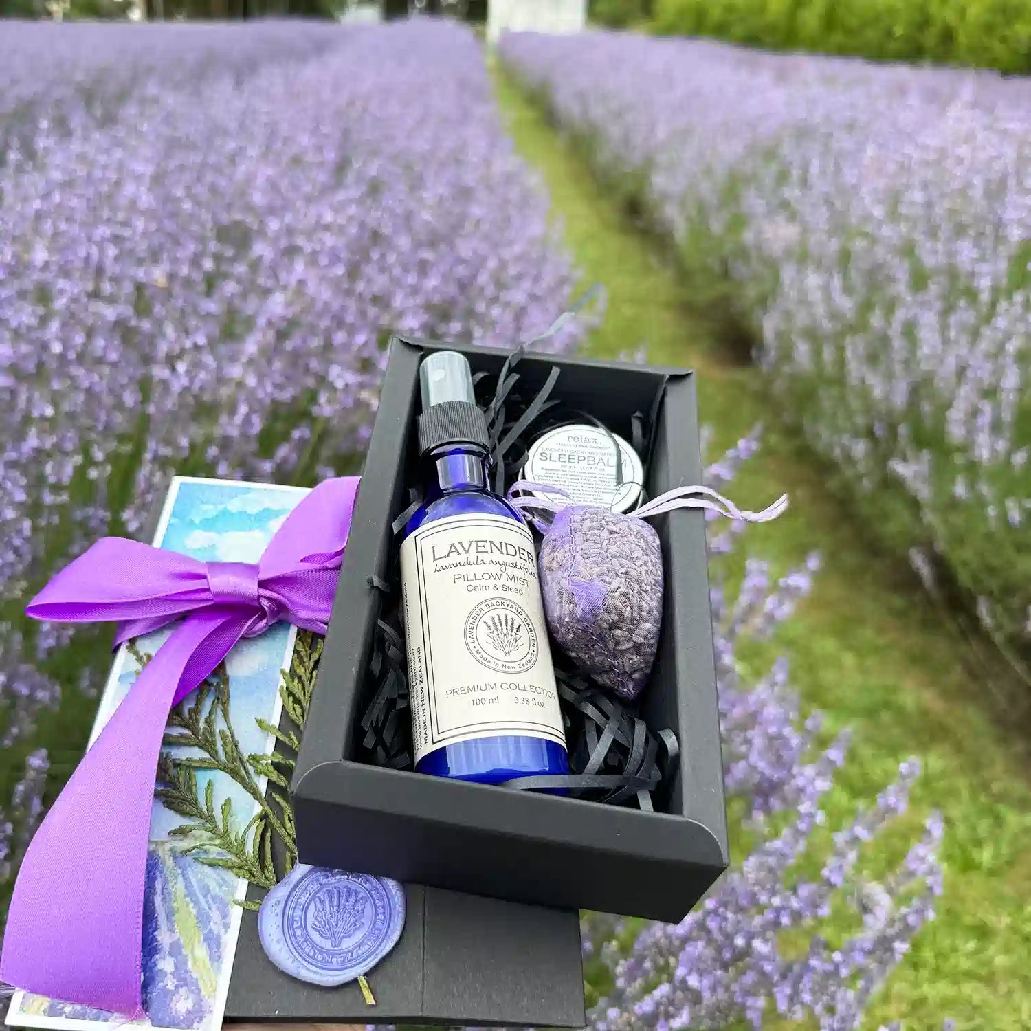 Peaceful Good Night's Sleepwell Gift Box featuring products such as Lavender Sleep Balm, Lavender Sleepwell Pillow Mist, Dried Lavender Sachet, and a Lavender Field Bookmark, with a lavender field background in New Zealand.