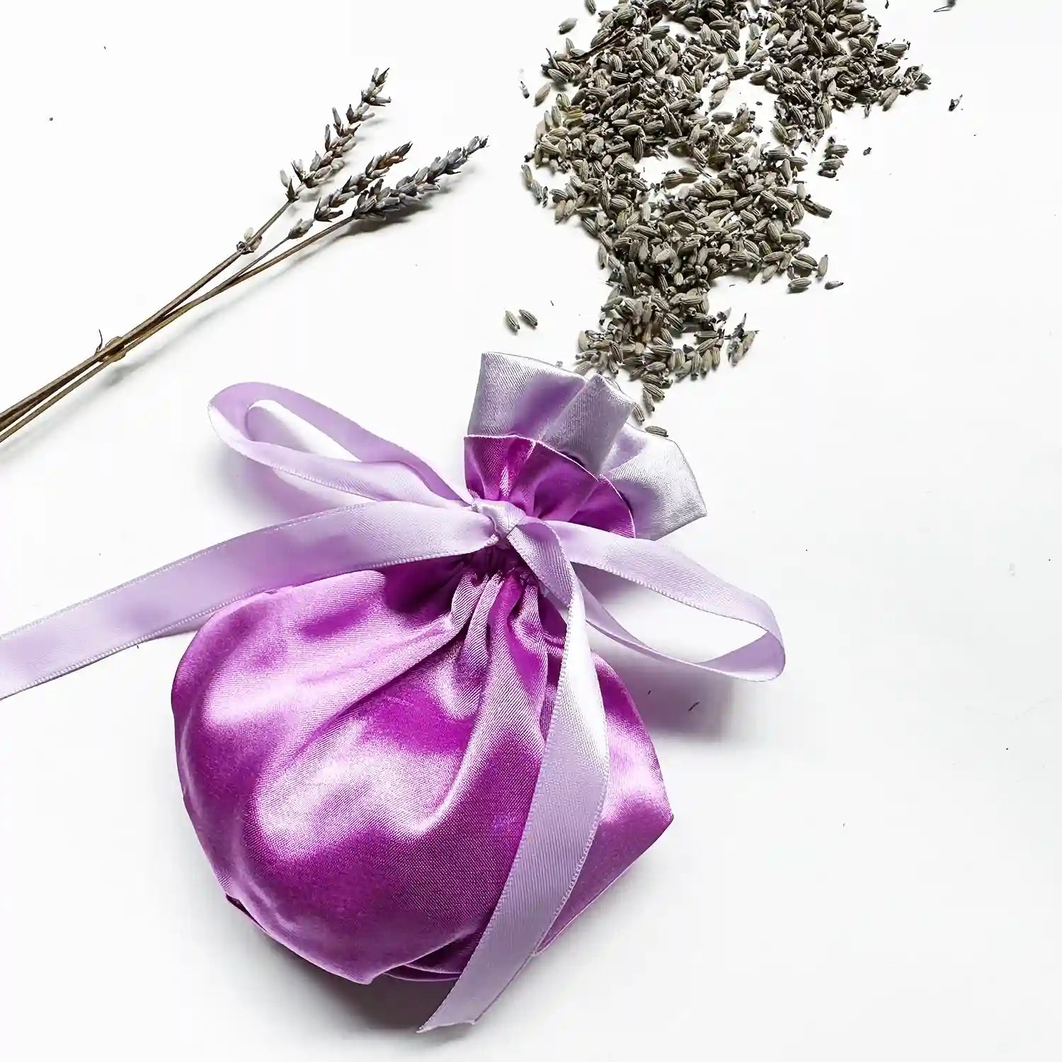 Sachet bag filled with lavender against a decorative background of lavender rubbings and dried lavender flowers.