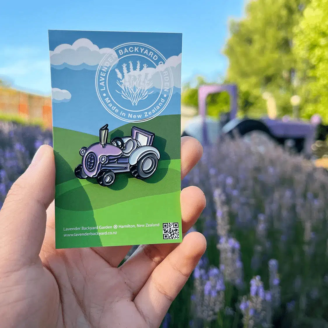 Close-up view of Purple Tractor Enamel Pin, designed in New Zealand, against the backdrop of NZ Lavender Farm, Lavender Backyard Garden, featuring a lavender field, farm shed, and purple tractor.