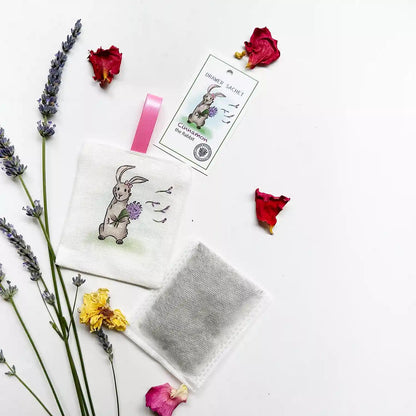 A scented linen sachet featuring Cinnamon the Rabbit, surrounded by dried lavender flowers and rose petals, perfect for closets and wardrobes.