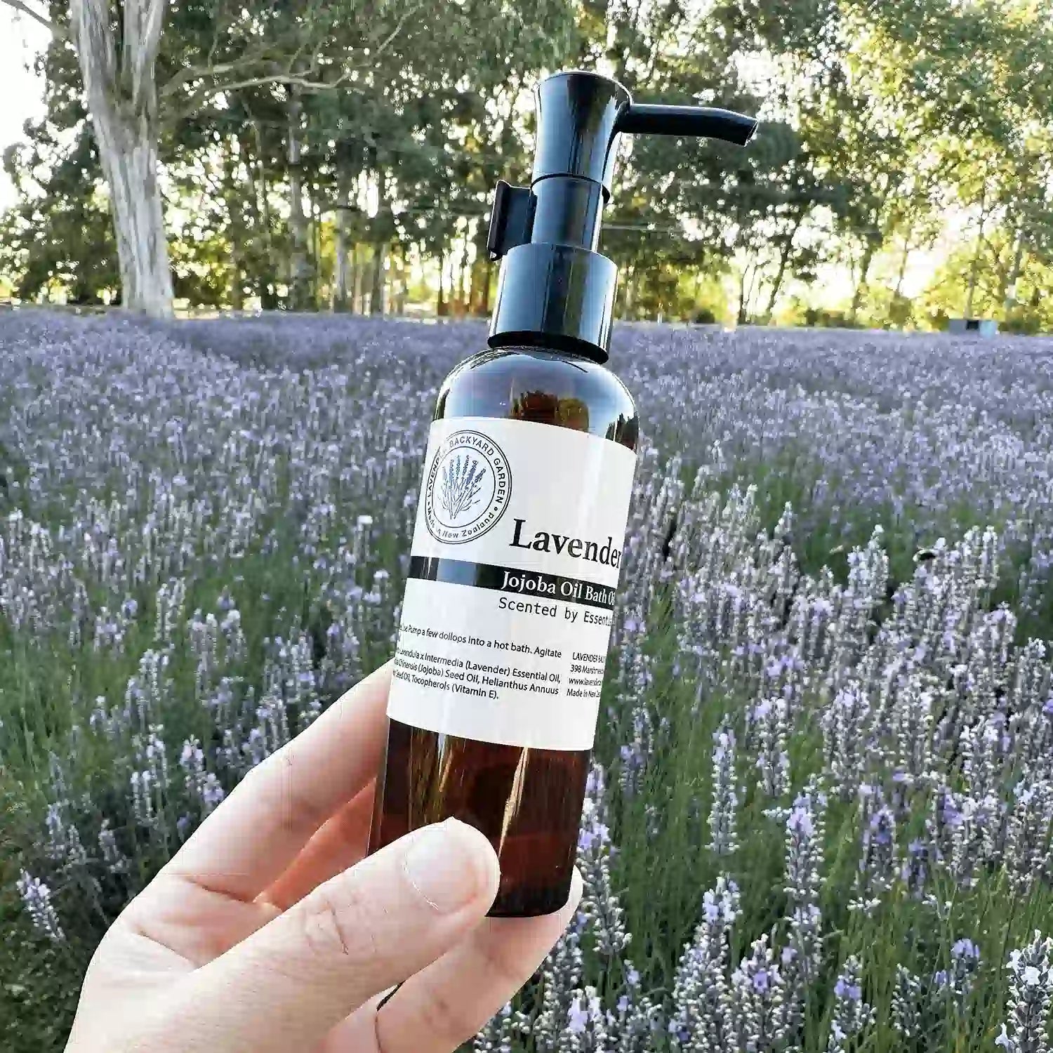 Soothe & Relax Lavender Bath Oil held by hand against rows of lavender at sunset at Lavender Backyard Garden.