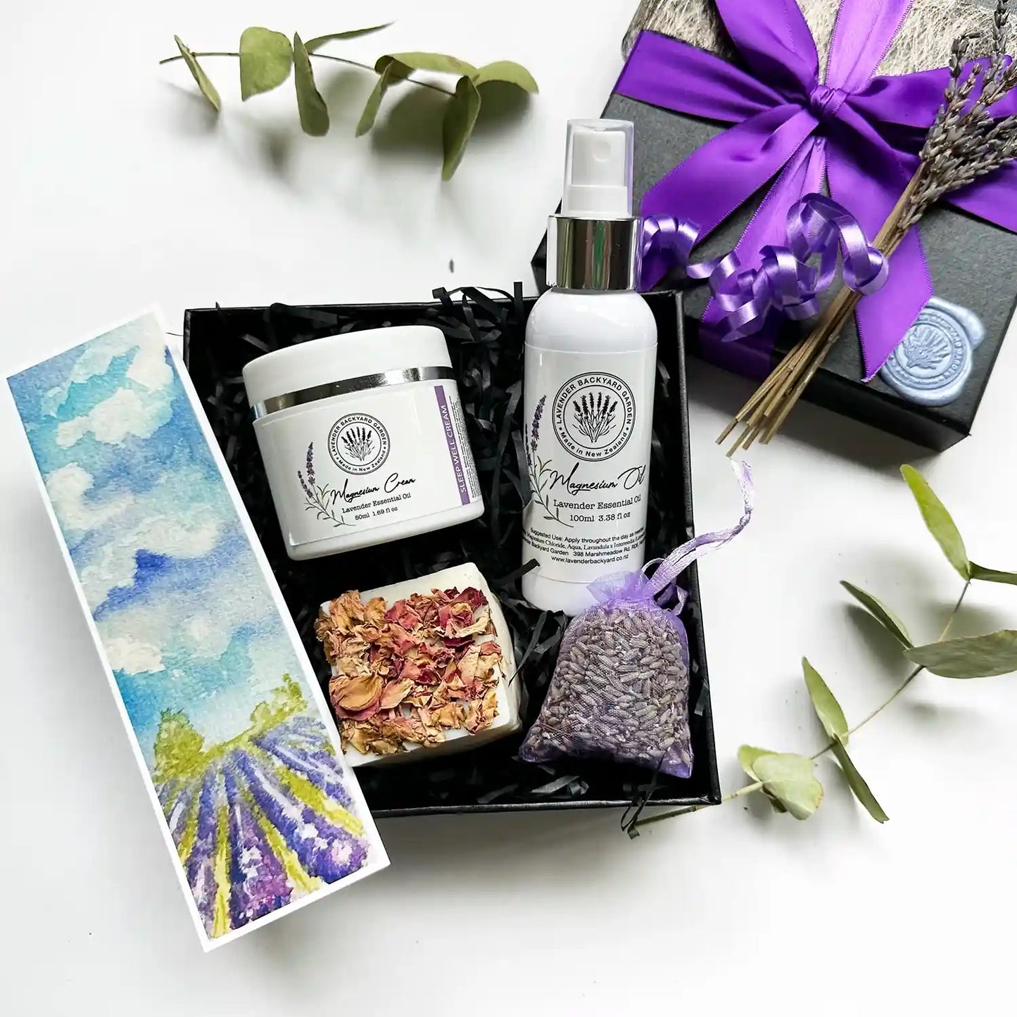 Release Stress Gift Ideas for Best Friend Female, wrapped in a purple ribbon gift box, featuring handcrafted lavender essential oil soap (assorted), lavender magnesium sleep cream, lavender magnesium oil sprays, dried lavender sachet, and lavender field bookmark, elegantly arranged for relaxation and comfort.