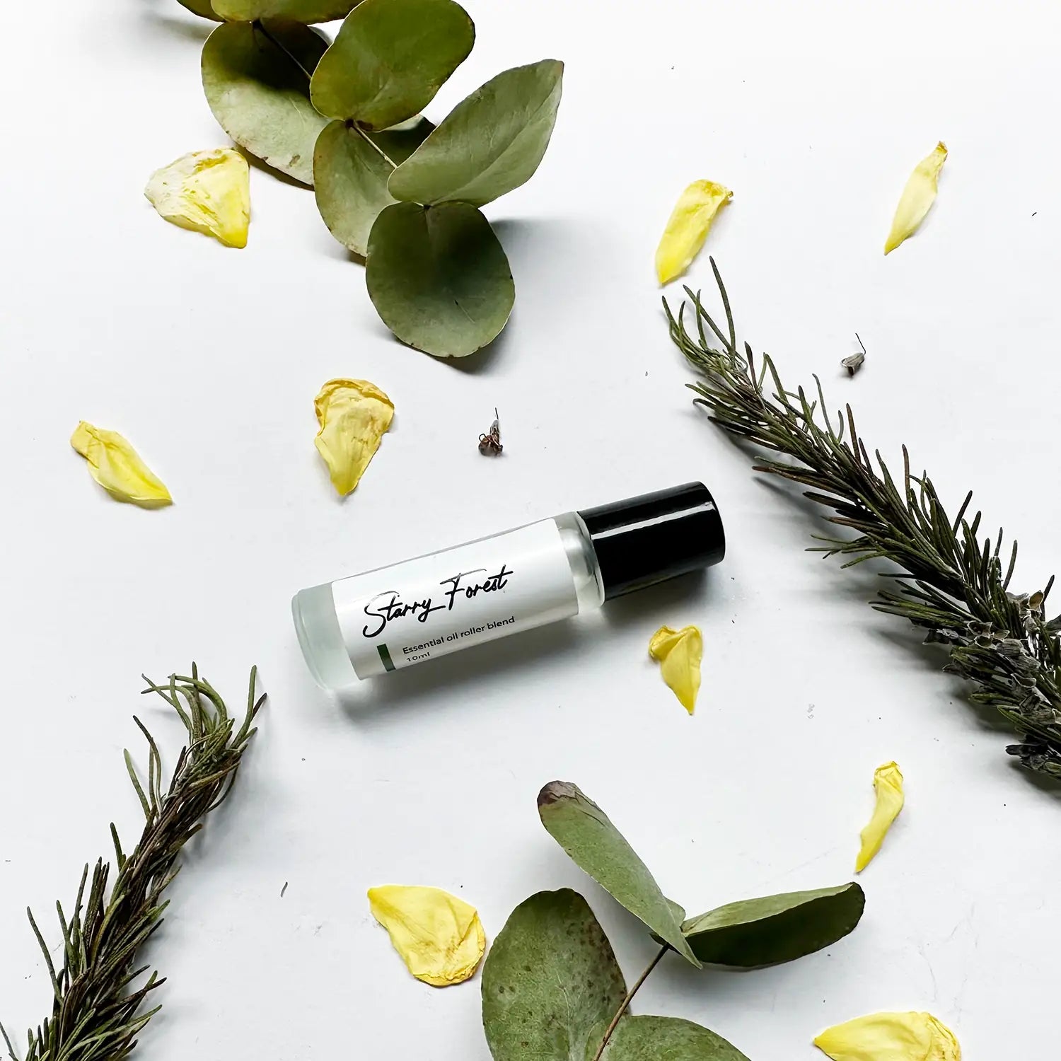 Starry Forest Essential Oil Roller Blend surrounded by rosemary sprigs, yellow roses, and eucalyptus leaves, perfect for spicy scent lovers.