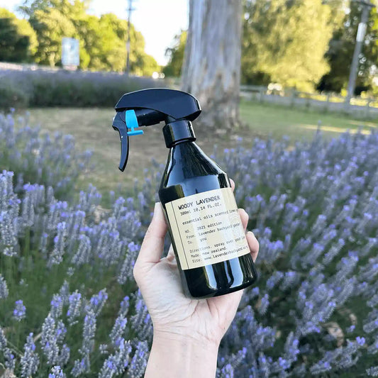 Holding Sweet Amber Lavender Linen Spray by hand against a purple lavender field and eucalyptus trees at Lavender Backyard Garden, NZ lavender farm.