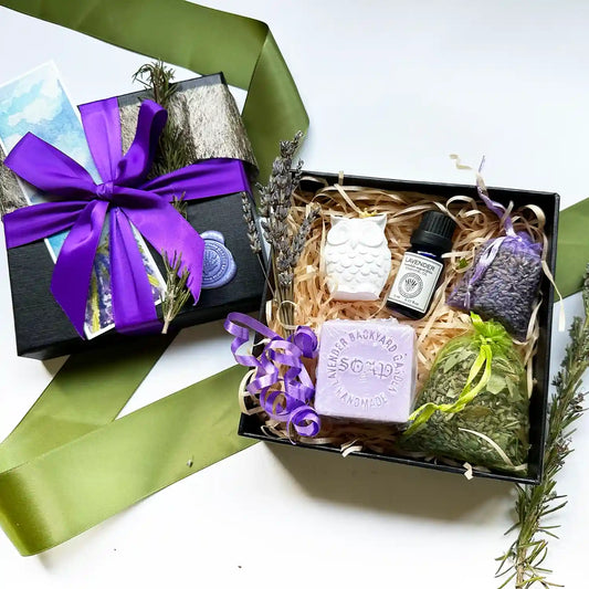 Thinking of You Aromatherapy Gift Set containing lavender sachets, handmade soap, lavender essential oil, and an aroma stone, beautifully wrapped in a purple ribbon with a black gift box."