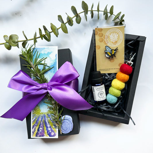 Missing You Cute Gift Set in a black gift box with a purple ribbon, featuring a bee badge, lavender essential oil, felt diffuser, dried rosemary, and a lavender field bookmark."