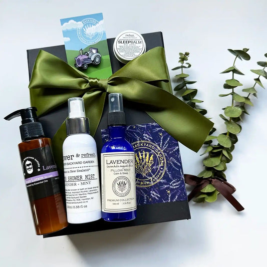 Gentleman’s Serenity Gift Box featuring men's body oil, after shower mist, pillow mist, and sleep balm scented with lavender essential oils, alongside tractor badges, displayed in a black gift box with a green ribbon background.