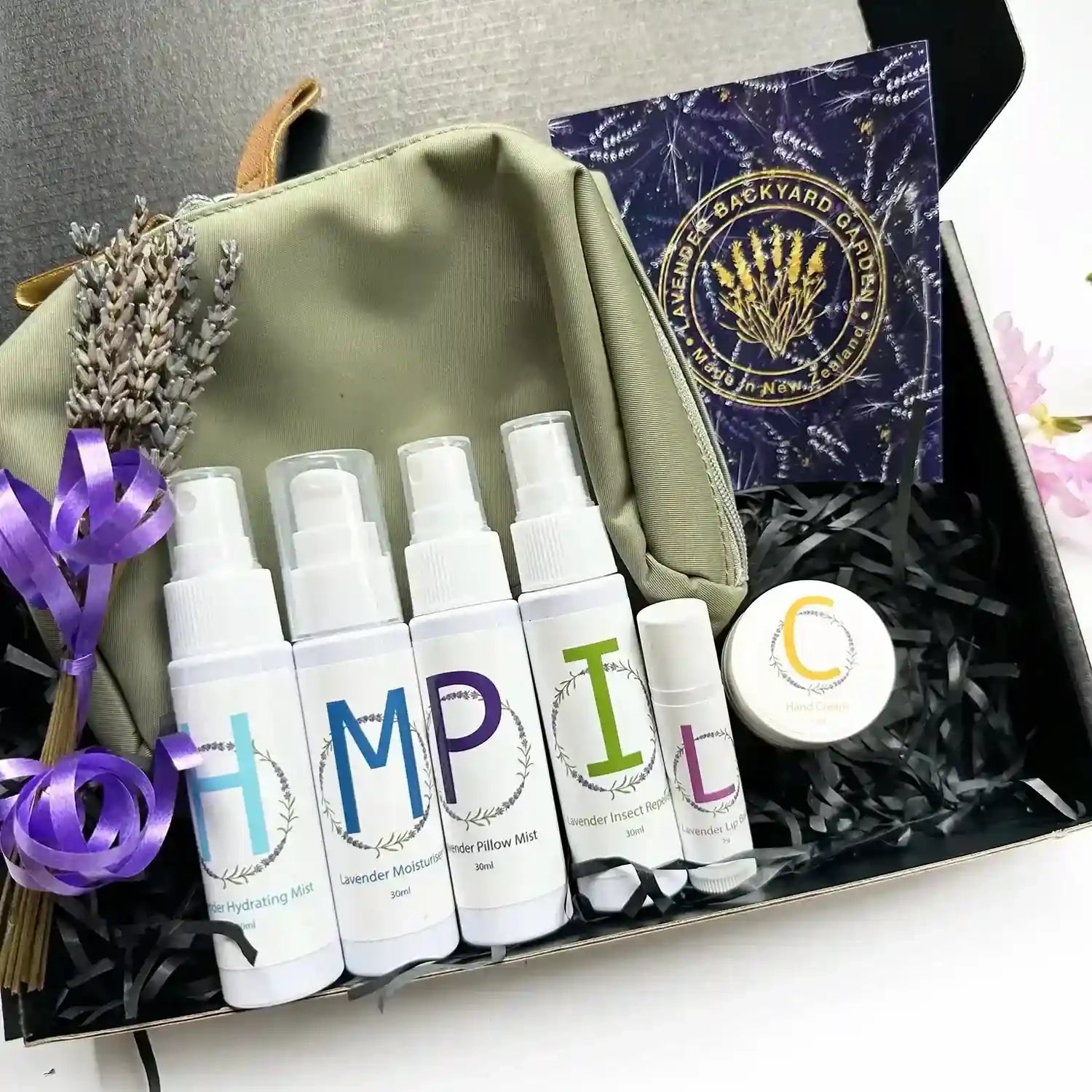 Essential oil scented travel self-care kit including lavender pillow mist, hydrating face mist, natural insect repellent, moisturizer lotion, hand cream, and lip balm in an earthy green toiletry bag.