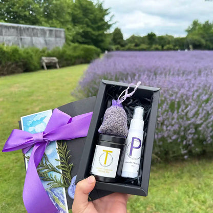 Ultimate Relax Gift Set for Mother's Day featuring Lavender Sleep Spray (Travel Size 30ml), Lavender & Chamomile Herbal Tea - Loose Leaf (Travel Size), Dried Lavender Sachet, and Lavender Field Bookmark, held by hand against the backdrop of a purple lavender field at Lavender Backyard Garden, NZ.