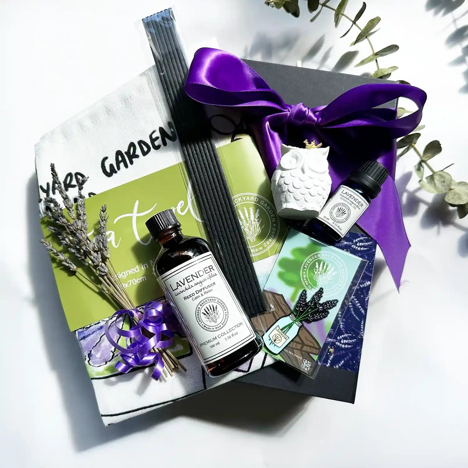 Luxury Mum Appreciation Gifts featuring a reed diffuser, lavender essential oils, aroma stone, farm-designed tea towel, farm savior fridge magnet, all wrapped with a purple ribbon, accompanied by mini dried lavender flowers and a lavender field bookmark.