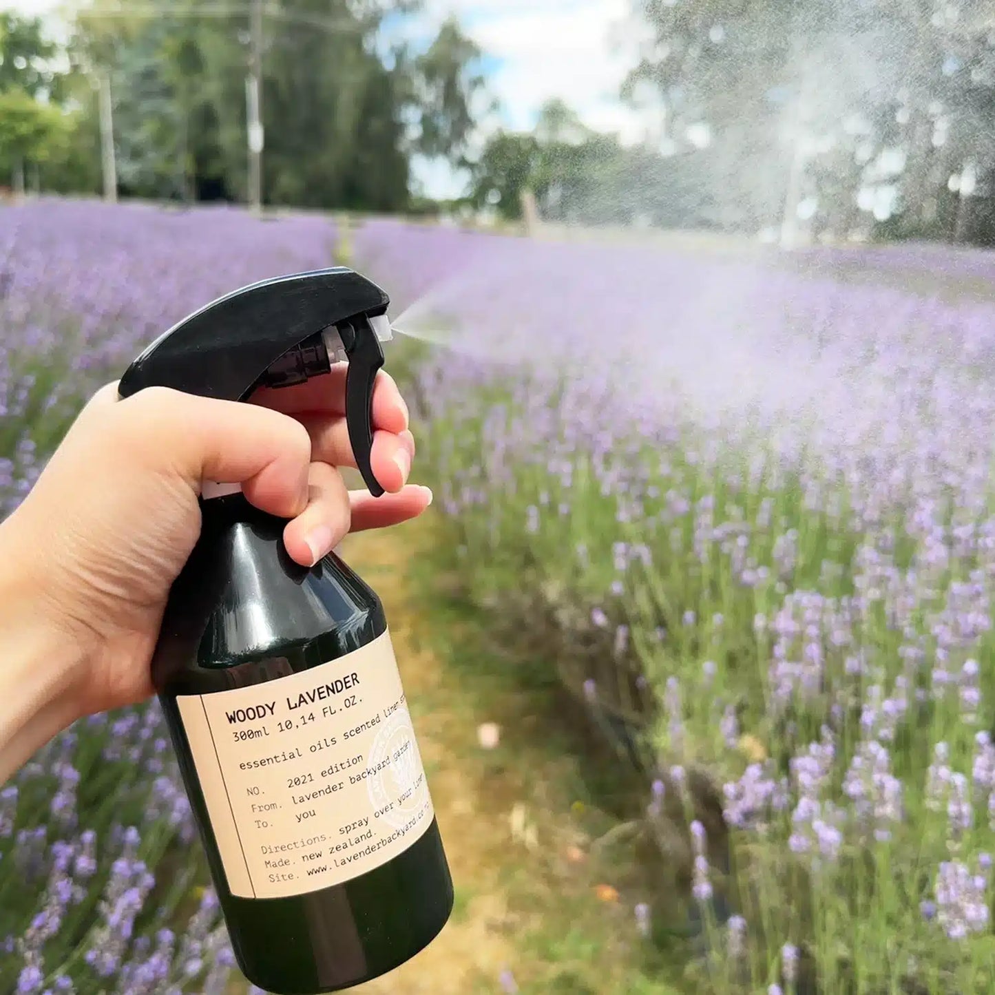 A bottle of woody lavender linen spray, scented with essential oil, placed among a vibrant lavender field at Lavender Backyard Garden in New Zealand.