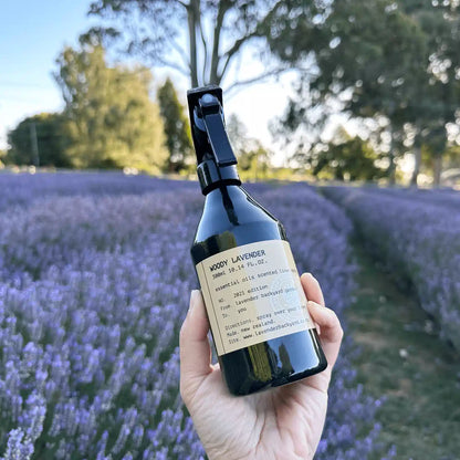 Woody Lavender Linen Spray, held in hand with a soft mist, set against a backdrop of lavender blooms at Lavender Backyard Garden, NZ.