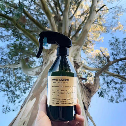 A bottle of woody lavender linen spray, scented with essential oil, held in hand against the background of eucalyptus trees at Lavender Backyard Garden in New Zealand.