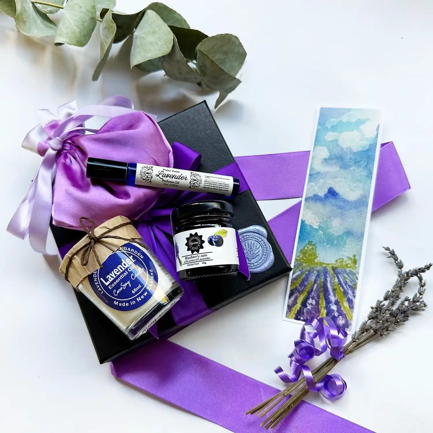 : A beautifully arranged "Xmas Present Ideas in Celebration" gift box featuring lavender light perfume, a lavender-scented soy candle, lavender blueberry jam, and a lavender sachet, all elegantly presented and infused with the soothing scent of lavender essential oil.